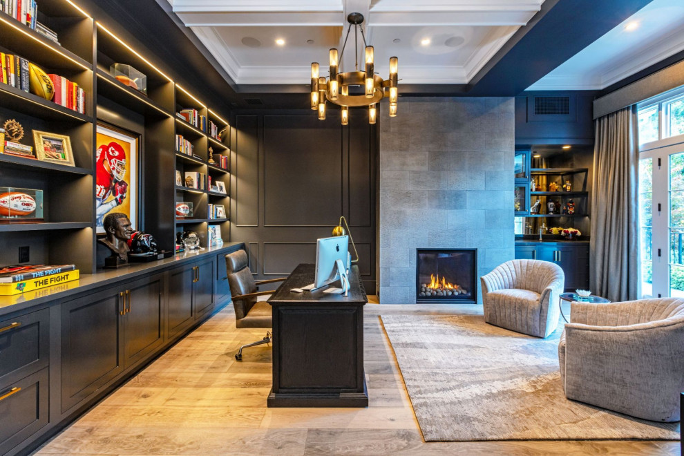 Mid-sized beach style home office in Los Angeles with black walls, light hardwood floors, a standard fireplace, a stone fireplace surround, a freestanding desk, beige floor, coffered and panelled walls.