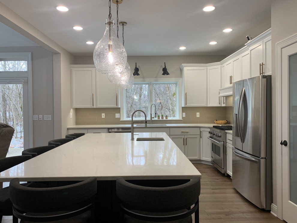 Inspiration for a large transitional l-shaped medium tone wood floor kitchen remodel in Milwaukee with recessed-panel cabinets, white cabinets, quartz countertops, beige backsplash, stainless steel appliances, an island and white countertops