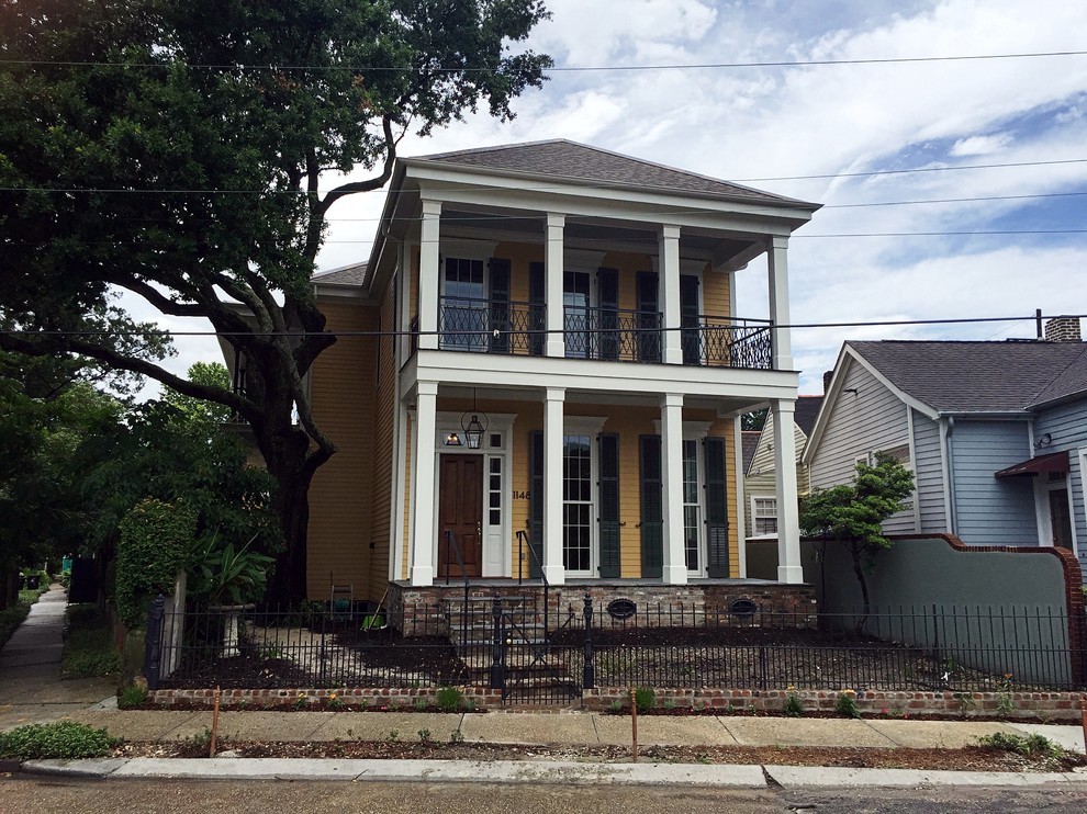 Photo of a mid-sized arts and crafts two-storey yellow exterior in New Orleans with vinyl siding and a hip roof.