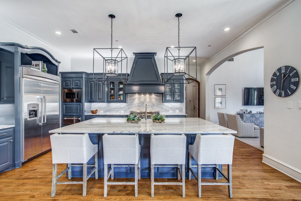 Photo of a transitional l-shaped kitchen in Dallas with raised-panel cabinets, blue cabinets, stainless steel appliances, medium hardwood floors, with island, brown floor and grey benchtop.