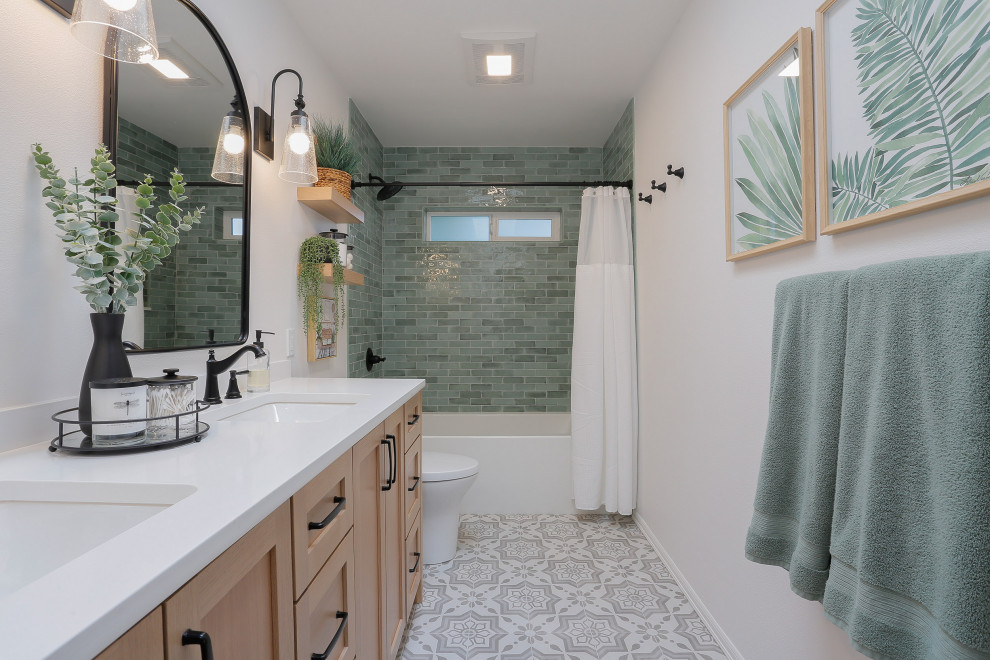 Photo of a mid-sized beach style kids bathroom in Seattle with shaker cabinets, light wood cabinets, an alcove tub, a shower/bathtub combo, a one-piece toilet, green tile, subway tile, white walls, porcelain floors, an undermount sink, engineered quartz benchtops, grey floor, a shower curtain, white benchtops, a double vanity and a built-in vanity.