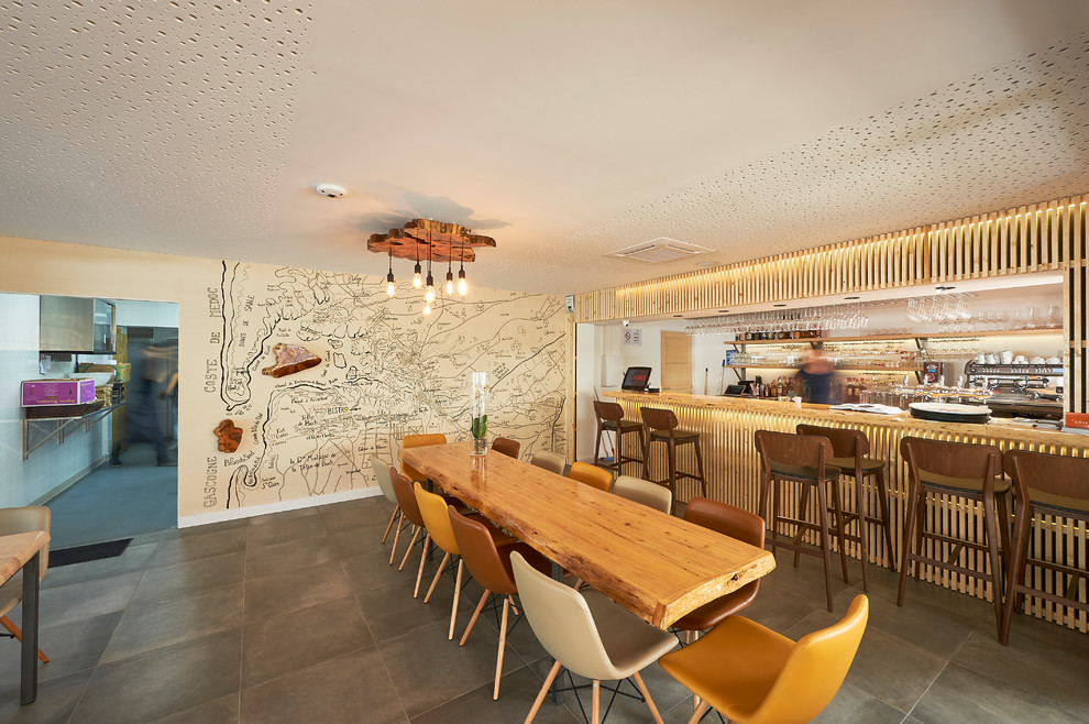 This is an example of a large beach style single-wall seated home bar in Bordeaux with ceramic floors, grey floor, open cabinets, light wood cabinets, wood benchtops, white splashback and beige benchtop.