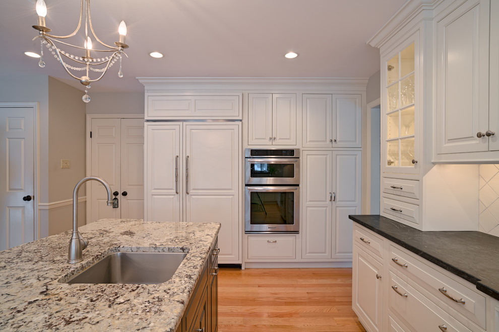 This is an example of a large traditional u-shaped open plan kitchen in Philadelphia with an undermount sink, raised-panel cabinets, white cabinets, soapstone benchtops, white splashback, mosaic tile splashback, stainless steel appliances, light hardwood floors and with island.