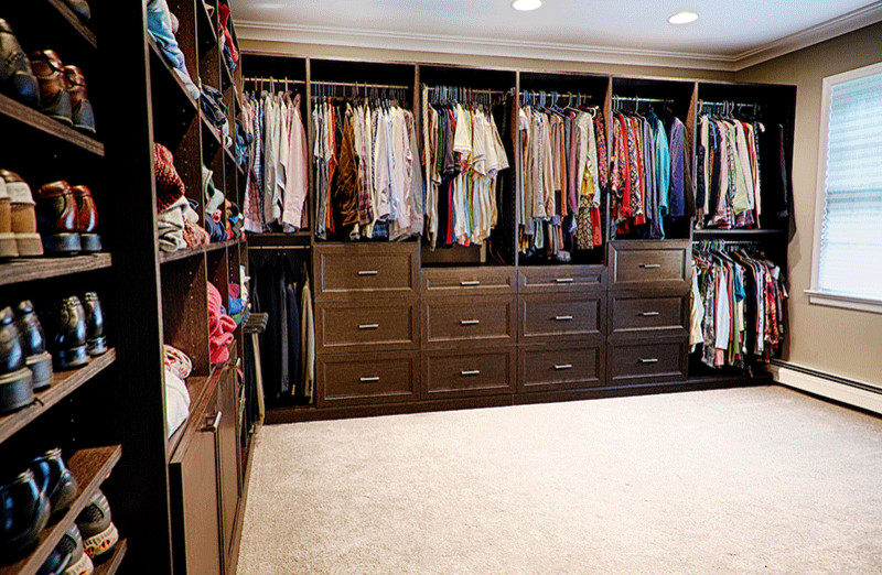 This is an example of a large traditional gender-neutral dressing room in Other with carpet, beige floor, recessed-panel cabinets and dark wood cabinets.