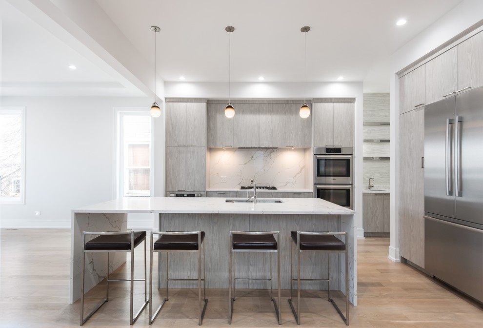 Large contemporary single-wall eat-in kitchen in Chicago with an undermount sink, flat-panel cabinets, light wood cabinets, quartzite benchtops, white splashback, stone slab splashback, stainless steel appliances, light hardwood floors, with island, multi-coloured floor and white benchtop.