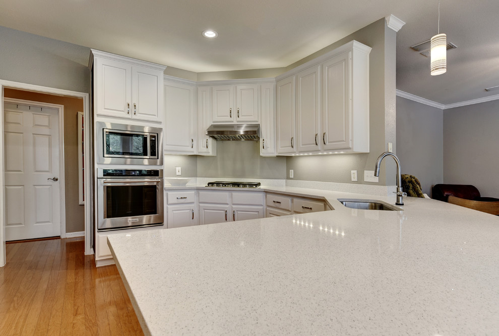 Example of a mid-sized transitional u-shaped light wood floor eat-in kitchen design in Austin with an undermount sink, white cabinets, quartz countertops, white backsplash, stone slab backsplash, stainless steel appliances, a peninsula and raised-panel cabinets
