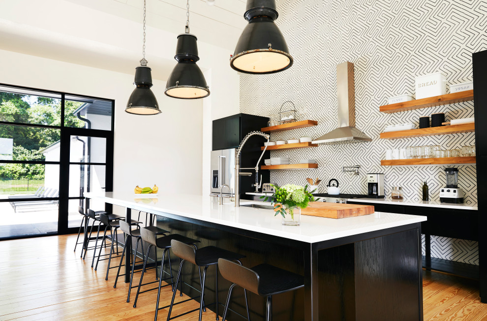 Example of a transitional light wood floor kitchen design with an undermount sink, flat-panel cabinets, black cabinets, multicolored backsplash, stainless steel appliances, an island and white countertops