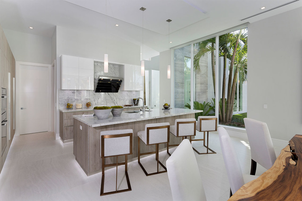 Photo of a beach style eat-in kitchen in Miami with a double-bowl sink, flat-panel cabinets, white cabinets, marble benchtops, grey splashback, marble splashback, with island, grey floor and grey benchtop.