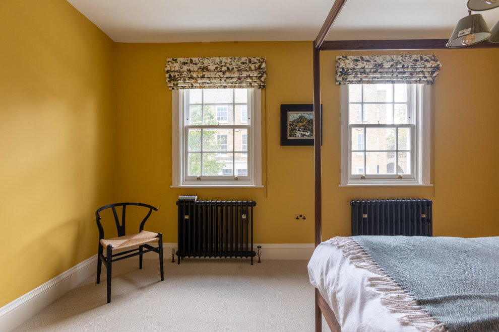 Design ideas for a mid-sized master bedroom in London with yellow walls, carpet, no fireplace and beige floor.