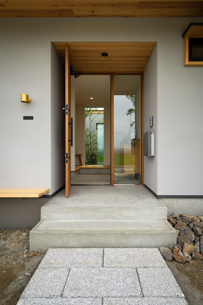 Nordisk inredning av en liten ingång och ytterdörr, med grå väggar, betonggolv, en enkeldörr, mellanmörk trädörr och grått golv