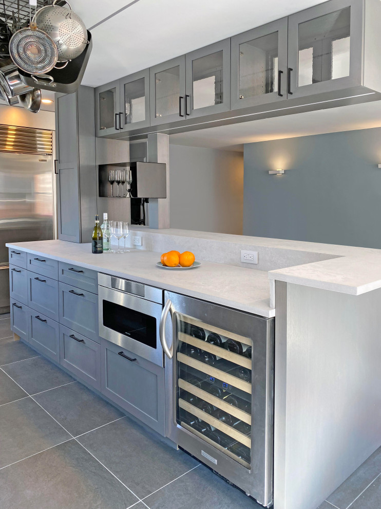 Photo of a mid-sized modern galley kitchen pantry in New York with glass-front cabinets, grey cabinets, quartzite benchtops, with island, white benchtop, a drop-in sink, white splashback, stone tile splashback, stainless steel appliances, ceramic floors and grey floor.
