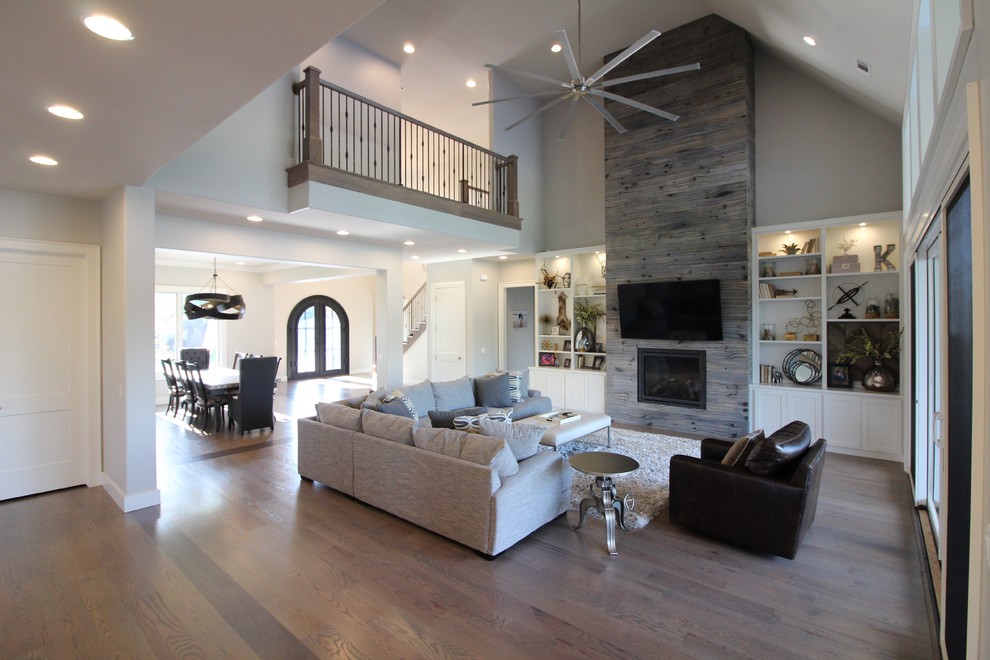 Transitional open concept medium tone wood floor and brown floor living room photo with beige walls, a standard fireplace, a wood fireplace surround and a wall-mounted tv