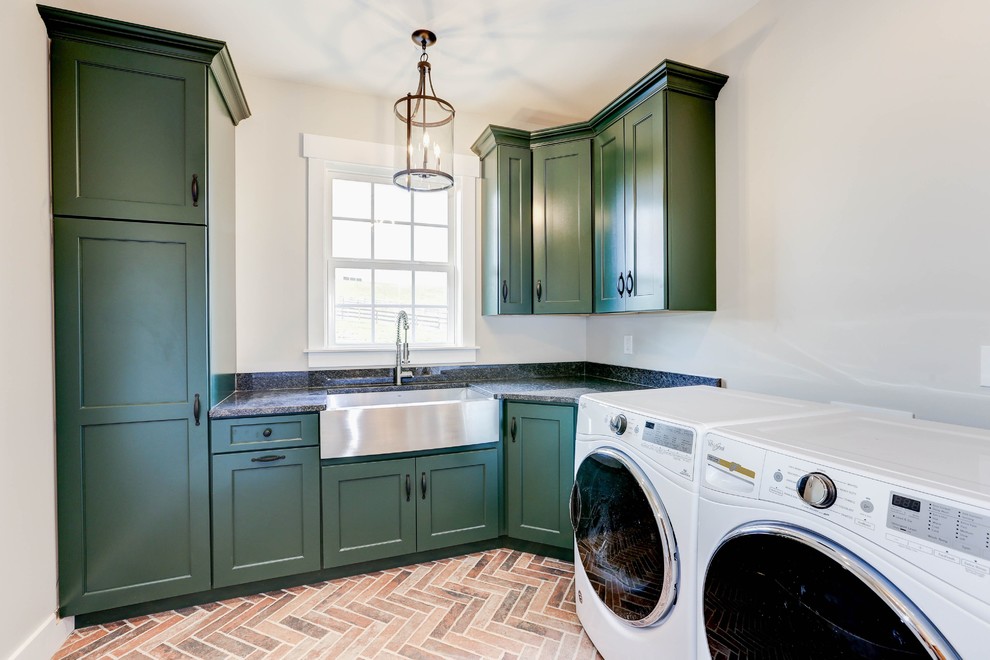 Inspiration for a transitional l-shaped laundry room in DC Metro with a farmhouse sink, shaker cabinets, green cabinets, a side-by-side washer and dryer, brown floor, grey benchtop and grey walls.