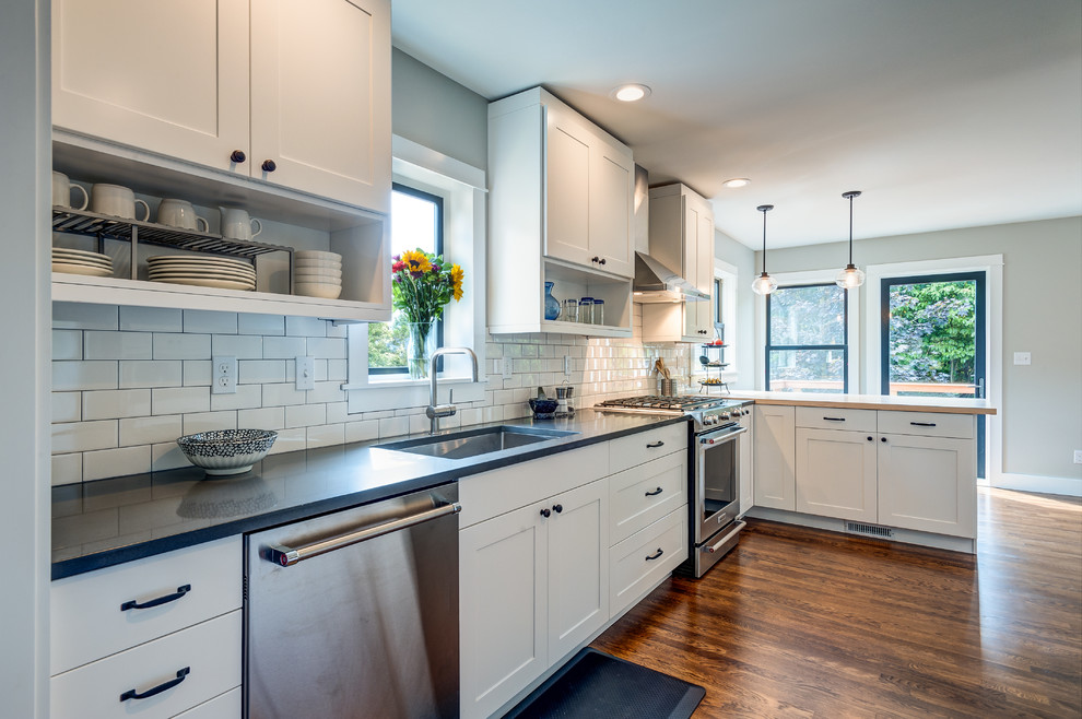 Design ideas for a mid-sized arts and crafts l-shaped eat-in kitchen in Seattle with an undermount sink, shaker cabinets, white cabinets, quartz benchtops, white splashback, subway tile splashback, stainless steel appliances, dark hardwood floors and a peninsula.