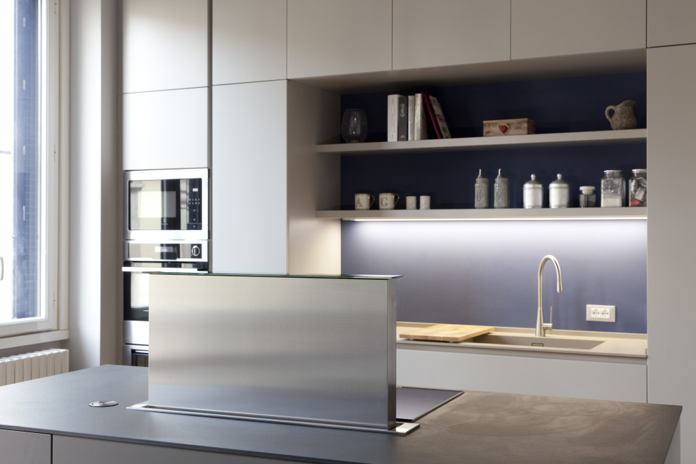 This is an example of a medium sized contemporary galley open plan kitchen in Milan with an integrated sink, beaded cabinets, grey cabinets, black appliances, light hardwood flooring, an island and grey worktops.