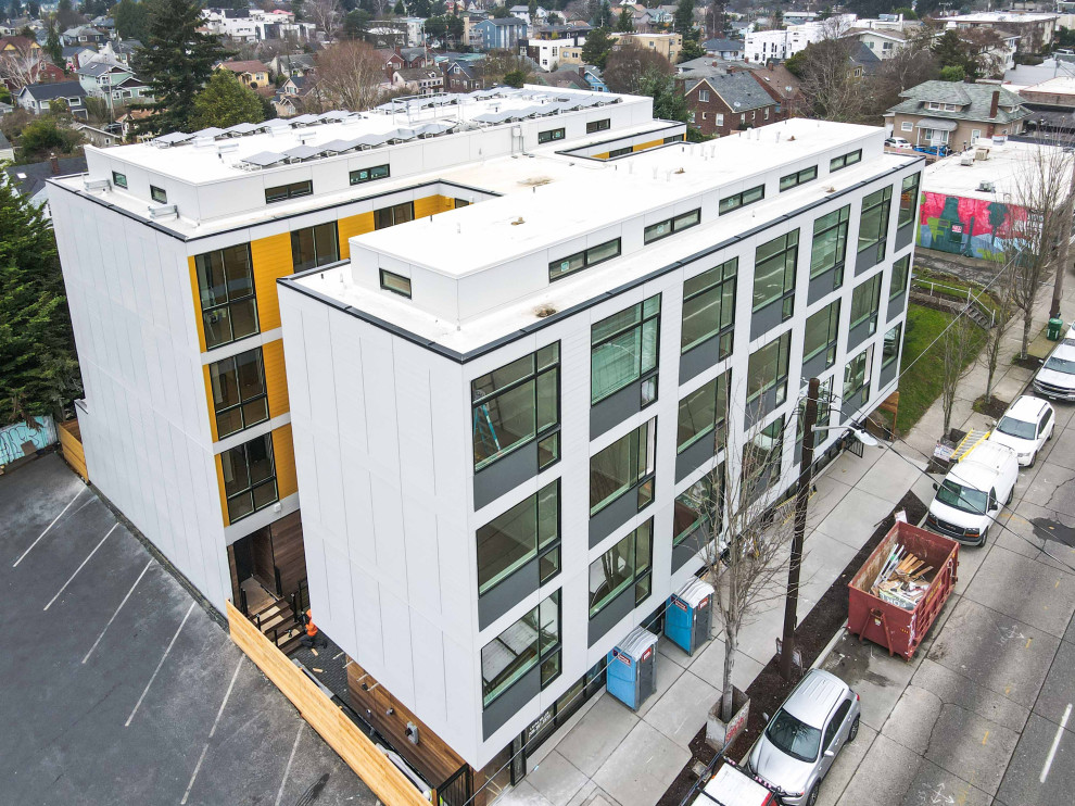 Expansive modern orange apartment exterior in Seattle with four or more storeys, concrete fiberboard siding, a flat roof, a mixed roof, a white roof and board and batten siding.