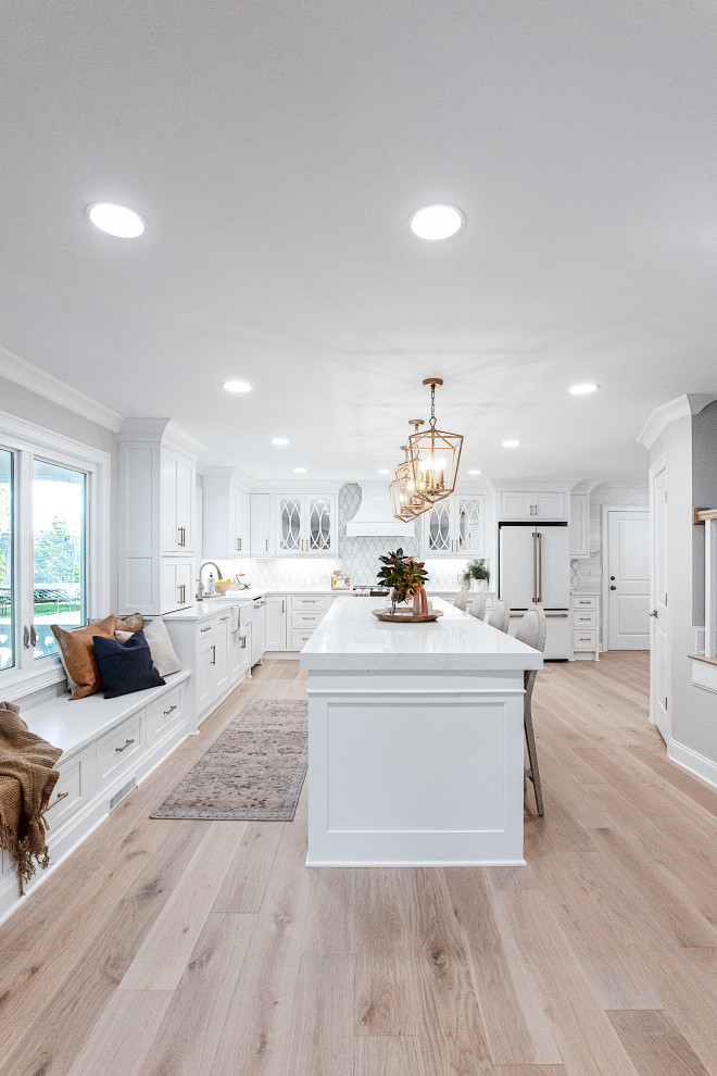 Example of a large classic l-shaped light wood floor and beige floor open concept kitchen design in Atlanta with an undermount sink, beaded inset cabinets, white cabinets, quartz countertops, white backsplash, marble backsplash, white appliances, an island and white countertops