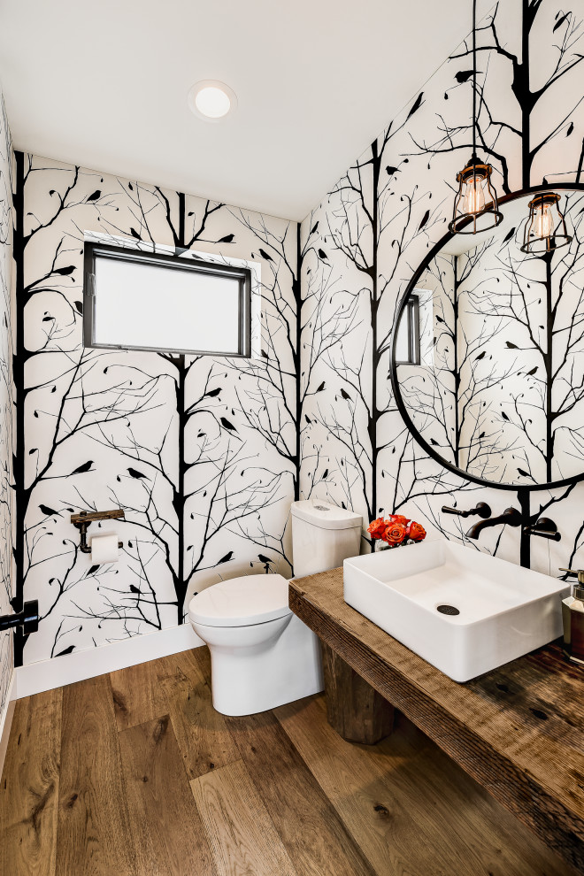 Inspiration for a small country powder room in Seattle with medium wood cabinets, a one-piece toilet, medium hardwood floors, a vessel sink, wood benchtops, a freestanding vanity and wallpaper.