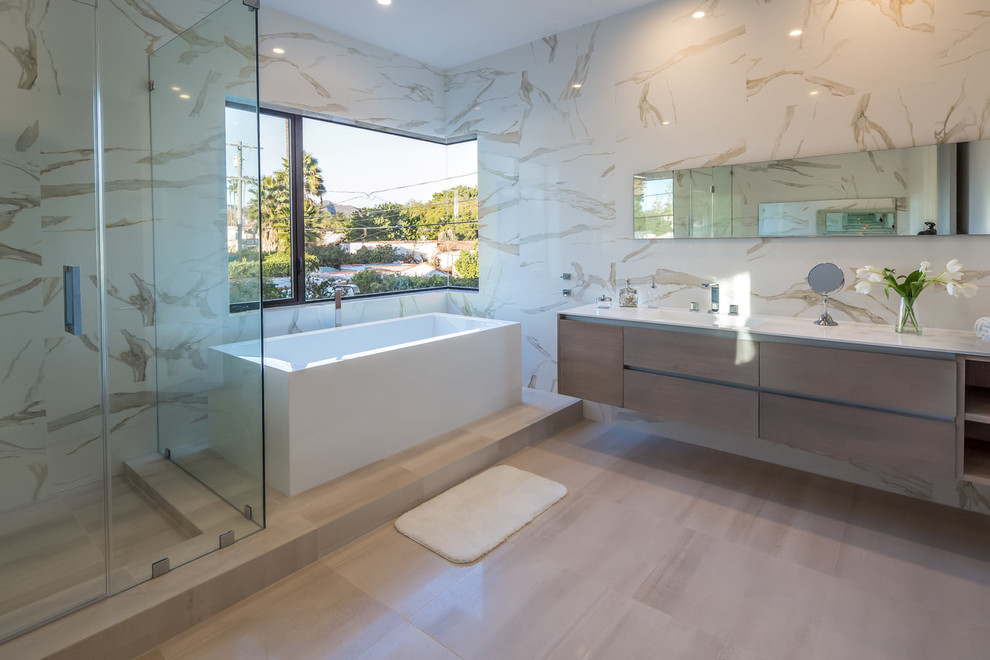 Photo of a large modern master bathroom in Los Angeles with flat-panel cabinets, light wood cabinets, a freestanding tub, a corner shower, beige tile, white tile, porcelain tile, multi-coloured walls, porcelain floors, an integrated sink and solid surface benchtops.