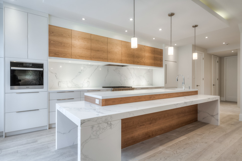 This is an example of a mid-sized modern galley eat-in kitchen in Toronto with an undermount sink, flat-panel cabinets, medium wood cabinets, quartzite benchtops, white splashback, stone slab splashback, panelled appliances, light hardwood floors, multiple islands, grey floor and white benchtop.