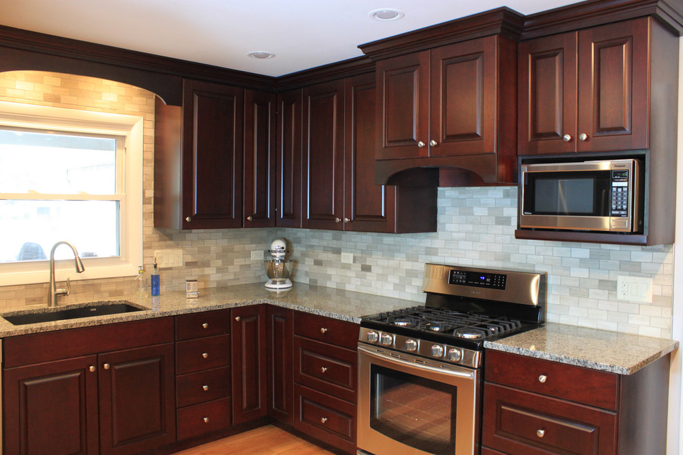 Mid-sized transitional u-shaped laminate floor eat-in kitchen photo with an undermount sink, raised-panel cabinets, dark wood cabinets, quartz countertops, gray backsplash, porcelain backsplash, stainless steel appliances and no island