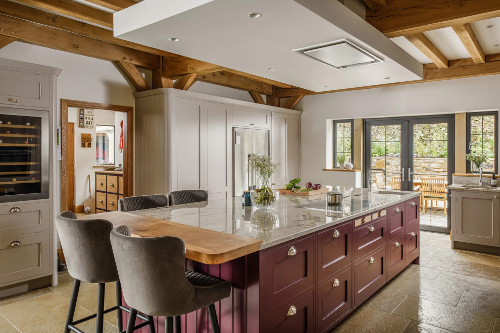 Inspiration for a large country l-shaped open plan kitchen in Manchester with a belfast sink, shaker cabinets, beige cabinets, granite worktops, beige splashback, ceramic splashback, black appliances, limestone flooring, an island, beige floors, beige worktops, a drop ceiling and a feature wall.