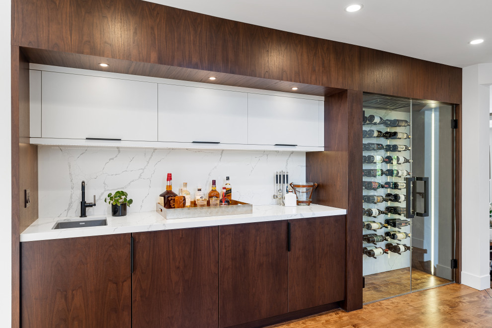 Photo of an expansive contemporary single-wall home bar in Los Angeles with a drop-in sink, flat-panel cabinets, dark wood cabinets, quartz benchtops, white splashback, engineered quartz splashback, medium hardwood floors, brown floor and white benchtop.