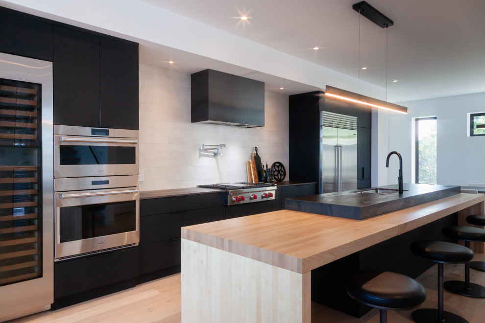 Photo of a large modern single-wall kitchen/diner in Toronto with a double-bowl sink, flat-panel cabinets, black cabinets, white splashback, stainless steel appliances, an island and black worktops.