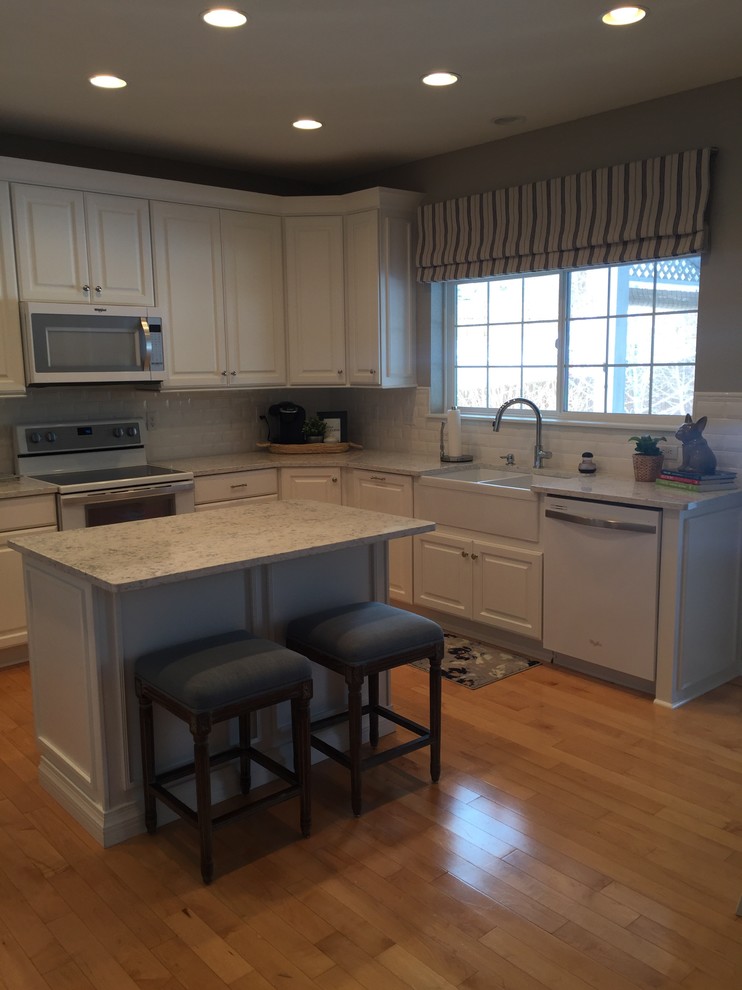 Large transitional u-shaped light wood floor and beige floor open concept kitchen photo in Denver with a farmhouse sink, raised-panel cabinets, white cabinets, quartz countertops, white backsplash, ceramic backsplash, white appliances and an island