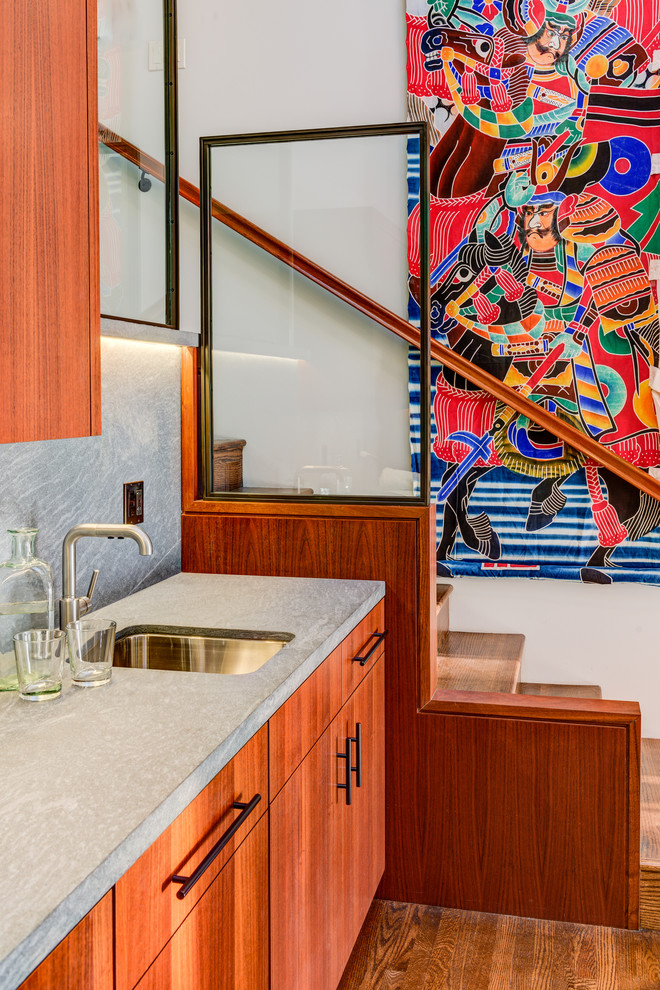 This is an example of a contemporary single-wall wet bar in San Francisco with an undermount sink, flat-panel cabinets, medium wood cabinets, grey splashback, medium hardwood floors, concrete benchtops and brown floor.