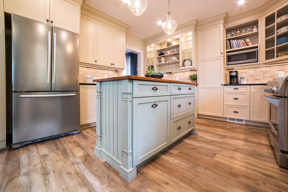 Mid-sized traditional separate kitchen in New York with a farmhouse sink, recessed-panel cabinets, beige cabinets, soapstone benchtops, beige splashback, travertine splashback, stainless steel appliances, vinyl floors, with island, brown floor and black benchtop.