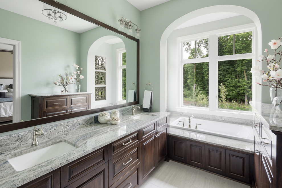 Photo of a traditional master bathroom in Minneapolis with raised-panel cabinets, dark wood cabinets, a drop-in tub, green walls, an undermount sink, grey floor and grey benchtops.