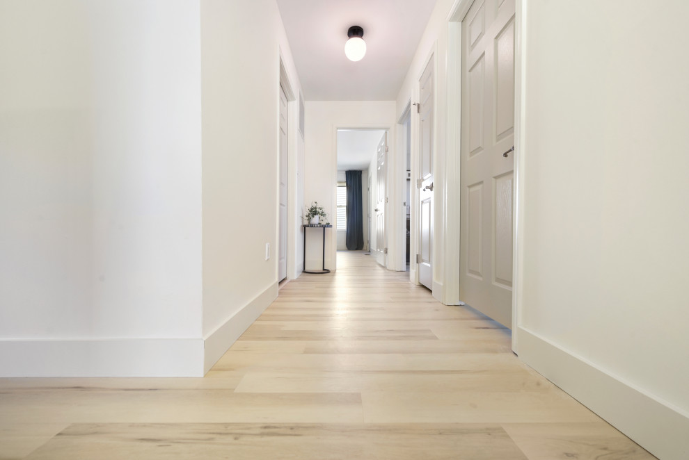 Cette image montre un couloir minimaliste de taille moyenne avec un mur blanc, un sol en vinyl et un sol beige.
