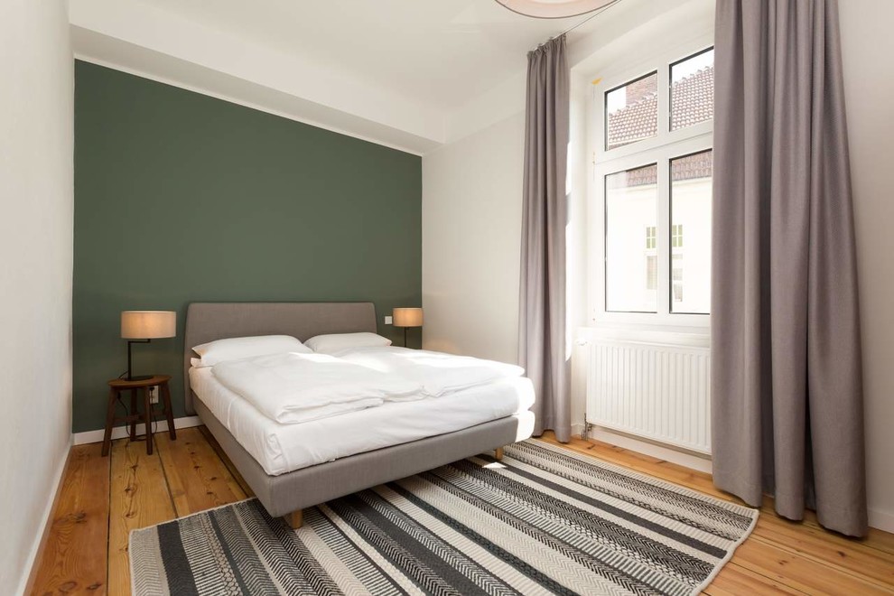 This is an example of a mid-sized master bedroom in Berlin with green walls, light hardwood floors and brown floor.