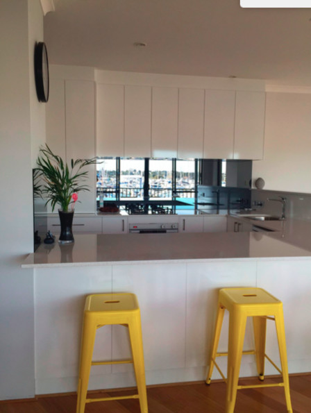 Photo of a small contemporary u-shaped separate kitchen in Perth with an undermount sink, white cabinets, quartz benchtops, glass sheet splashback, white appliances, light hardwood floors and brown floor.