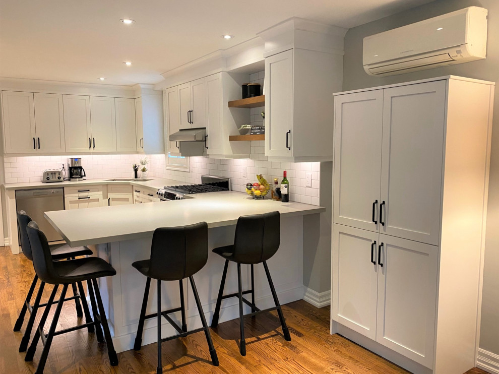 Mid-sized transitional u-shaped medium tone wood floor and brown floor open concept kitchen photo in Toronto with an undermount sink, shaker cabinets, white cabinets, quartz countertops, white backsplash, porcelain backsplash, stainless steel appliances, a peninsula and gray countertops
