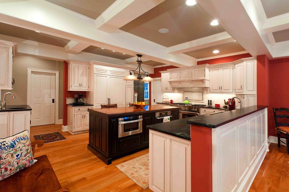 Mid-sized transitional u-shaped eat-in kitchen photo with raised-panel cabinets, white cabinets, soapstone countertops, beige backsplash and an island