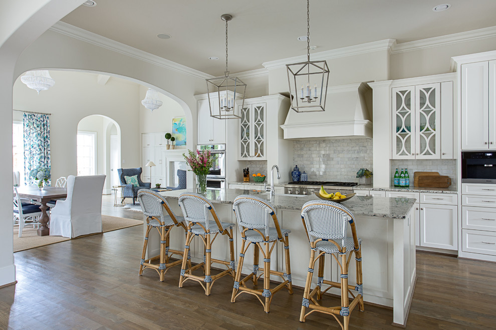 Photo of a beach style open plan kitchen in Dallas with white cabinets, grey splashback, marble splashback, stainless steel appliances, with island, brown floor, grey benchtop, medium hardwood floors and shaker cabinets.