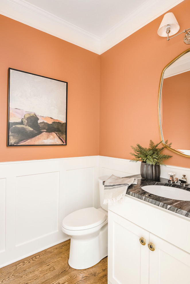 This is an example of a small transitional powder room in Charlotte with shaker cabinets, white cabinets, a two-piece toilet, orange walls, an undermount sink, marble benchtops, black benchtops, a built-in vanity and decorative wall panelling.