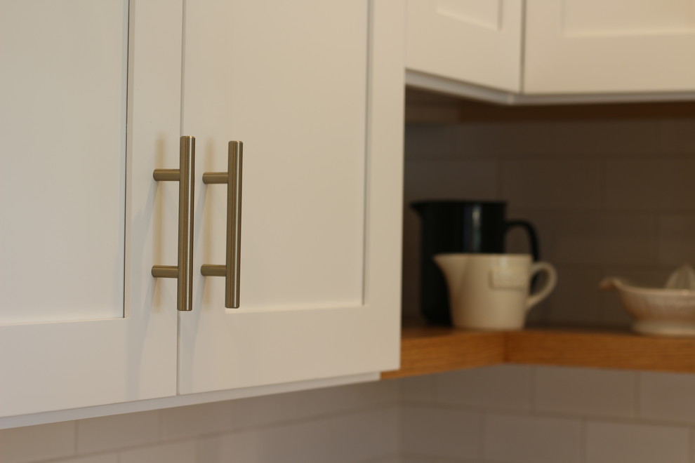 Inspiration for a mid-sized transitional u-shaped medium tone wood floor and brown floor enclosed kitchen remodel with a farmhouse sink, shaker cabinets, white cabinets, quartz countertops, white backsplash, subway tile backsplash, white appliances, no island and beige countertops