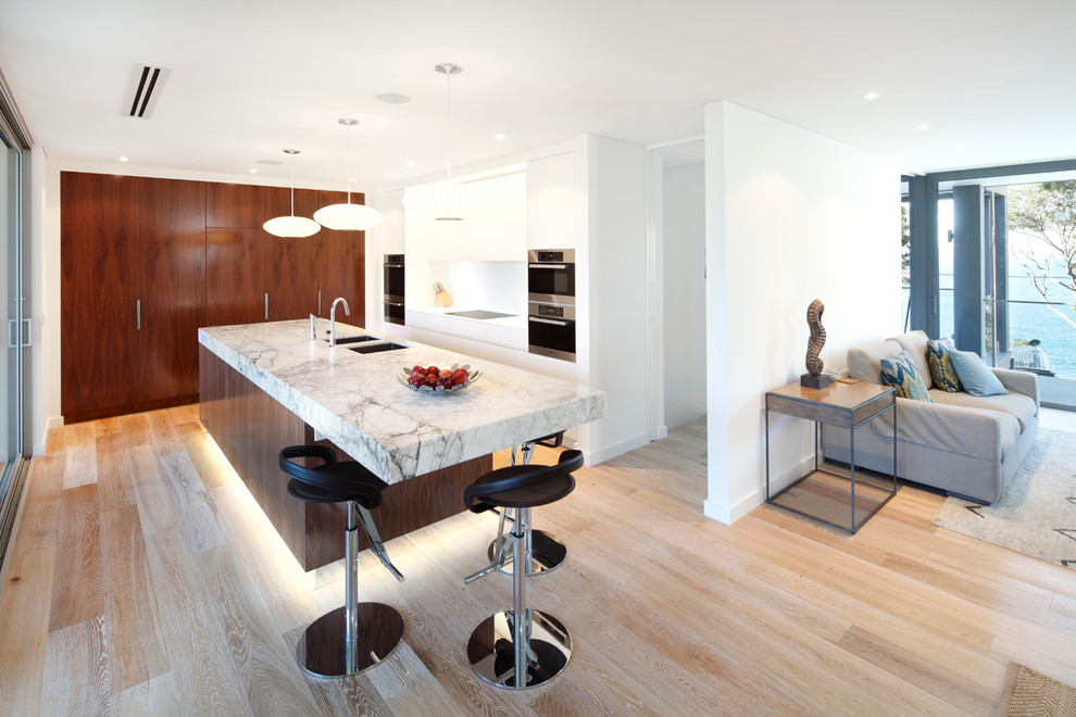 Mid-sized contemporary single-wall eat-in kitchen in Sydney with flat-panel cabinets, marble benchtops, a double-bowl sink, white cabinets, white splashback, stainless steel appliances, light hardwood floors and with island.