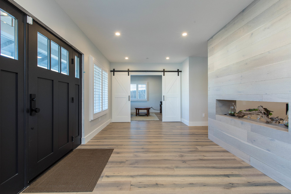 This is an example of a large transitional foyer in Los Angeles with grey walls, light hardwood floors, a single front door, a black front door and beige floor.