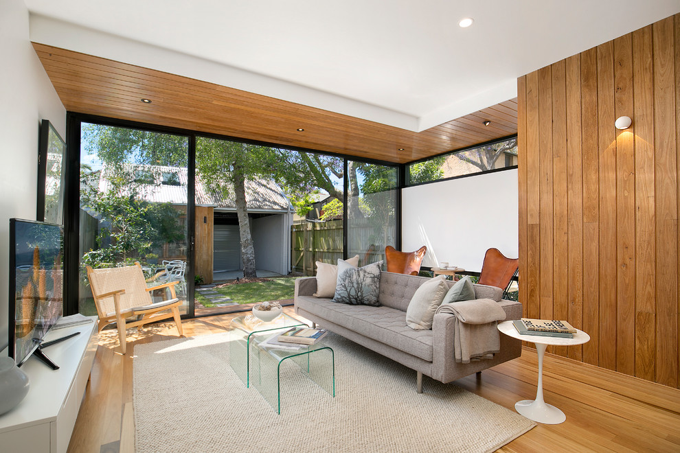 Photo of a mid-sized contemporary enclosed family room in Sydney with white walls, medium hardwood floors, a freestanding tv, no fireplace and brown floor.