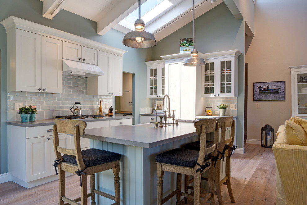 Design ideas for a mid-sized beach style l-shaped open plan kitchen in San Francisco with a farmhouse sink, shaker cabinets, white cabinets, quartz benchtops, blue splashback, subway tile splashback, panelled appliances, light hardwood floors and with island.