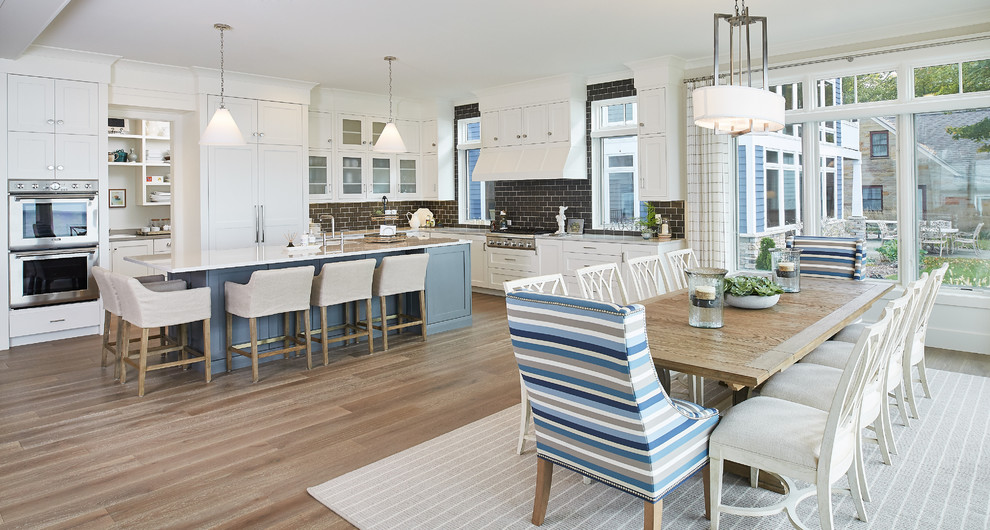 Design ideas for a large beach style l-shaped open plan kitchen in Grand Rapids with shaker cabinets, white cabinets, brown splashback, subway tile splashback, stainless steel appliances, medium hardwood floors and with island.