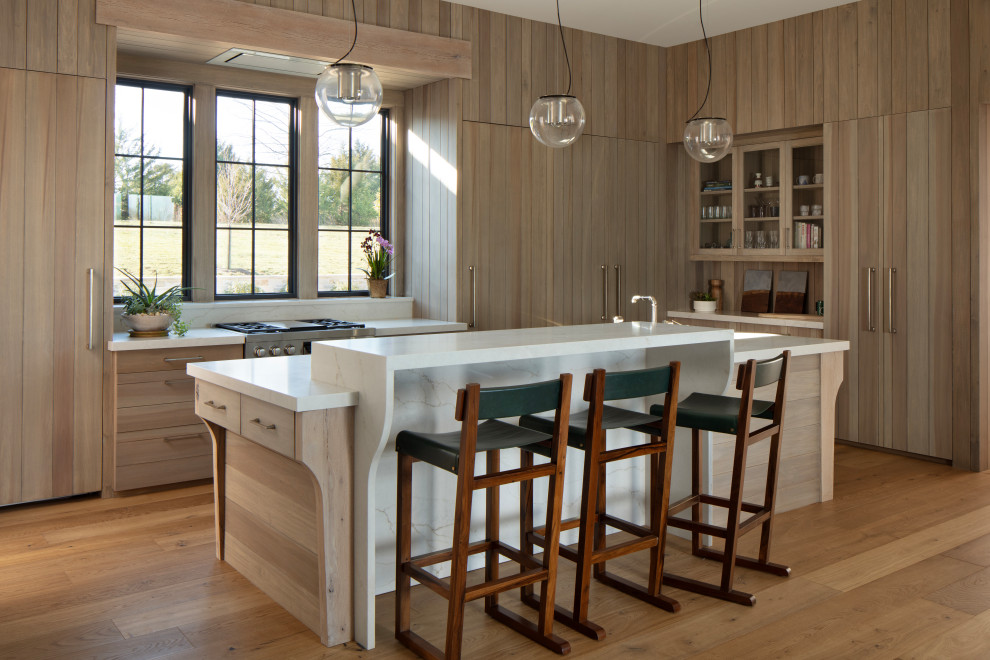 Foto på ett lantligt vit l-kök, med släta luckor, skåp i ljust trä, integrerade vitvaror, mellanmörkt trägolv, en köksö och brunt golv