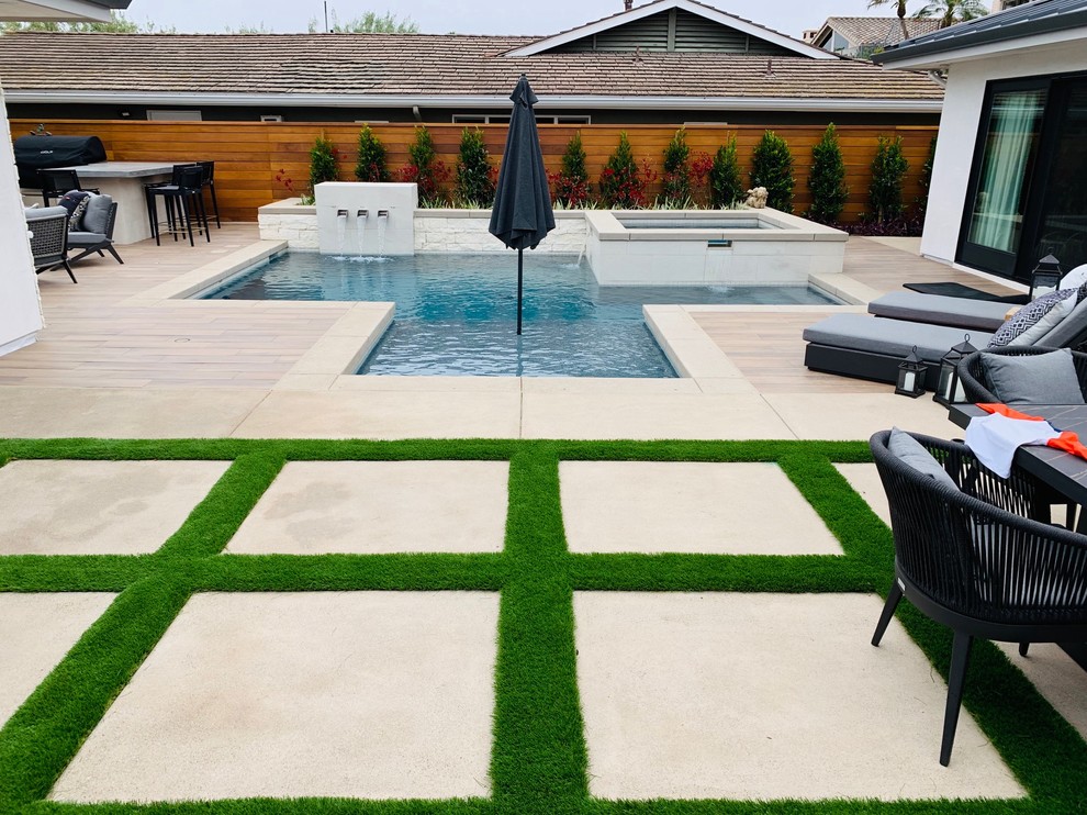 Mid-sized contemporary backyard custom-shaped pool in Orange County with a water feature and concrete pavers.