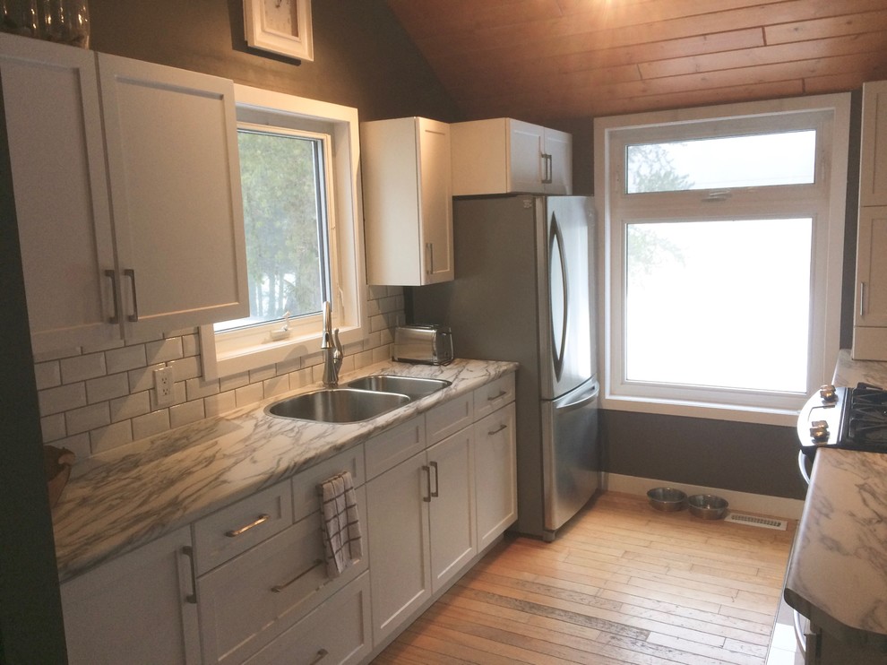 Eat-in kitchen - mid-sized transitional u-shaped light wood floor and brown floor eat-in kitchen idea with a drop-in sink, raised-panel cabinets, white cabinets, laminate countertops, white backsplash, ceramic backsplash, stainless steel appliances and a peninsula