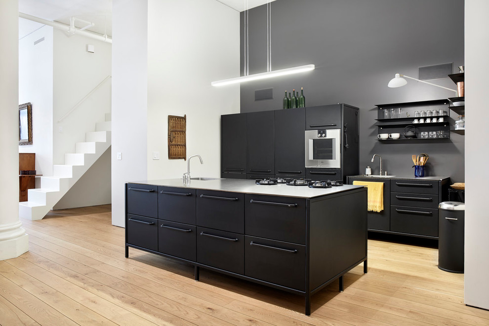 Design ideas for a contemporary galley kitchen in New York with flat-panel cabinets, black cabinets, black splashback, stainless steel appliances, light hardwood floors, with island, beige floor, grey benchtop, an integrated sink and stainless steel benchtops.