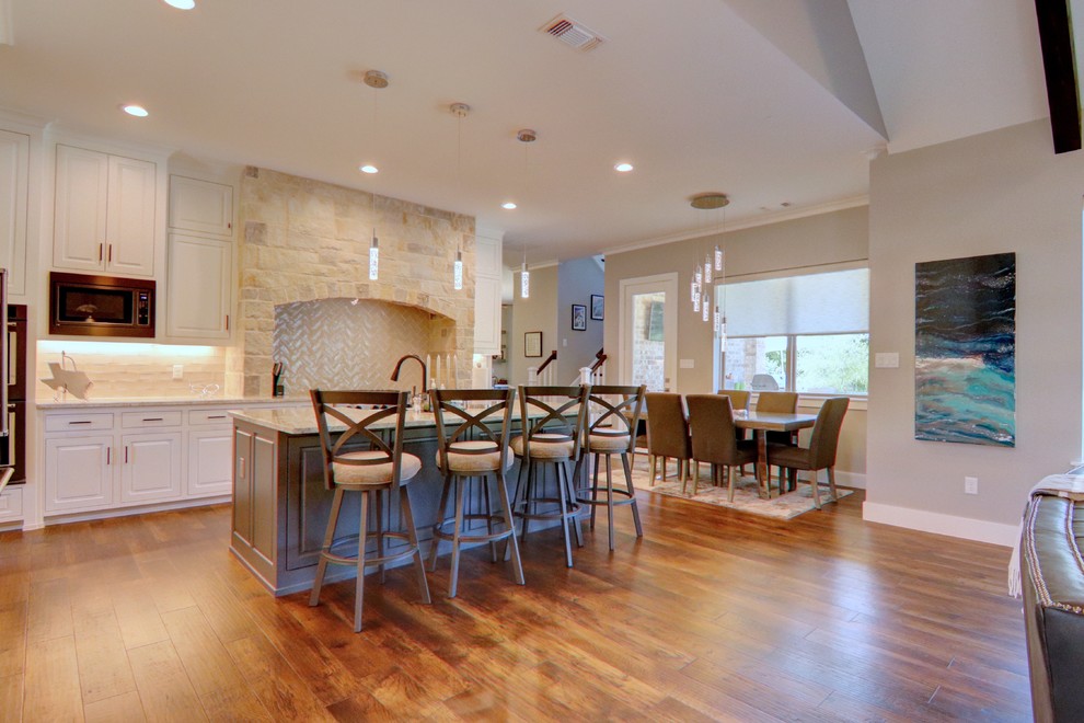 Example of a mid-sized transitional l-shaped medium tone wood floor and brown floor eat-in kitchen design in Dallas with a farmhouse sink, raised-panel cabinets, white cabinets, granite countertops, white backsplash, ceramic backsplash, colored appliances, an island and gray countertops